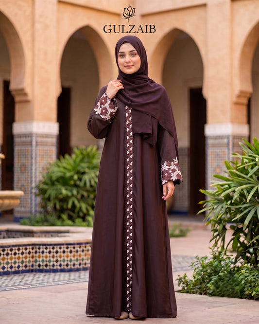 A woman wearing a dark brown abaya with floral-patterned sleeves and a matching hijab stands in front of an arched courtyard. The brand name 'GULZAIB' is displayed at the top.