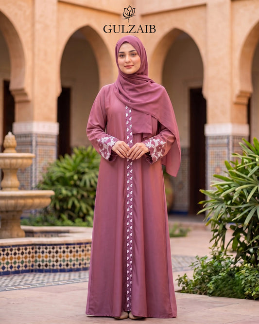 A woman wearing a dusty rose abaya with white floral embroidery and a matching hijab stands in front of a traditional courtyard with arches. The brand name 'GULZAIB' is displayed at the top.