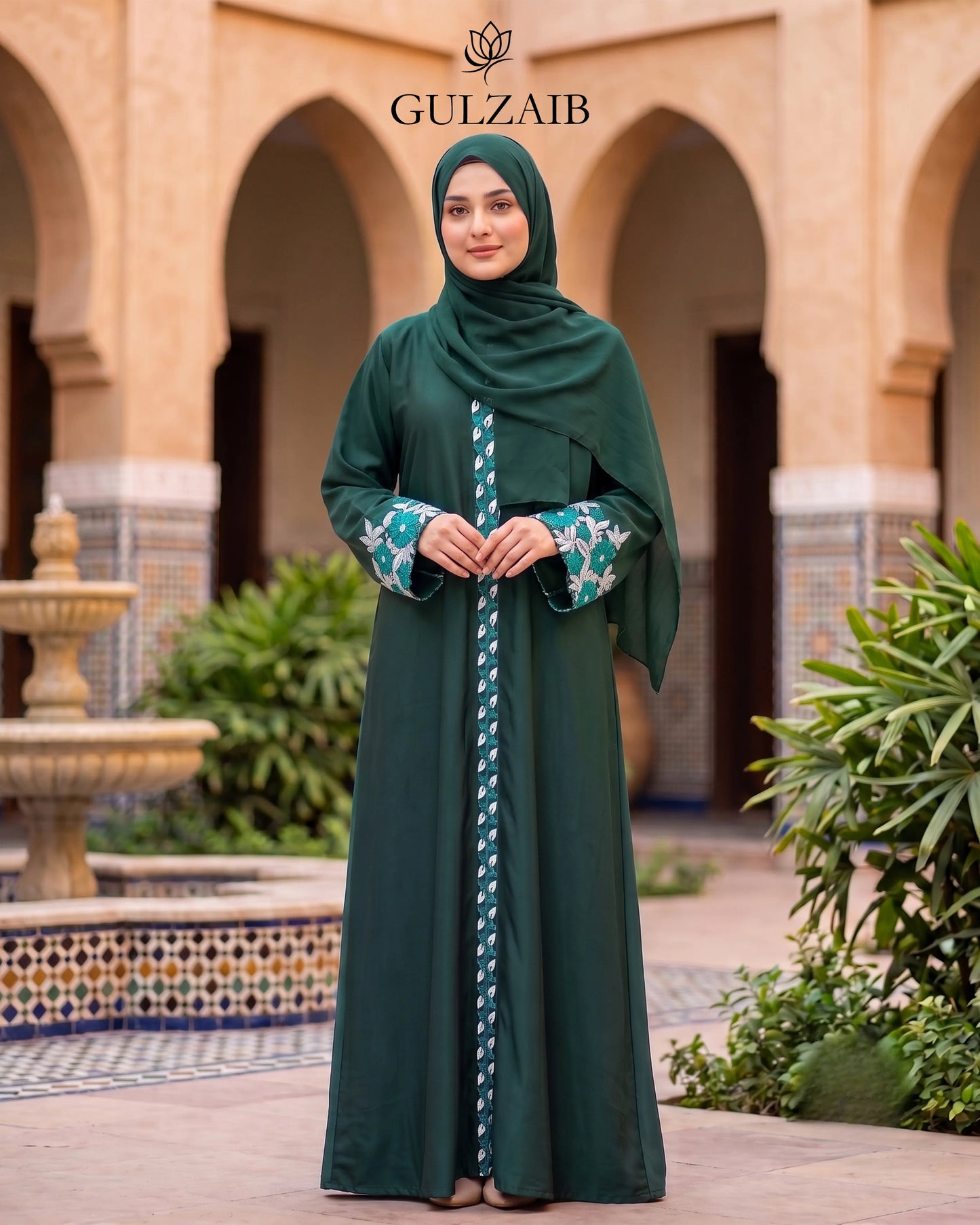 A woman wearing an emerald green abaya with a matching hijab and a decorative patterned inner lining, standing in front of a traditional courtyard with arches. The brand name 'GULZAIB' is displayed at the top.